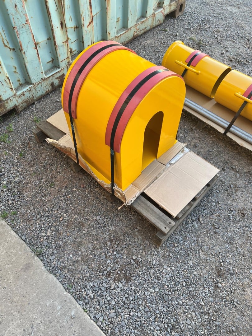 Yellow painted conveyor pulley guards with reflective banding, strapped to pallets in the yard