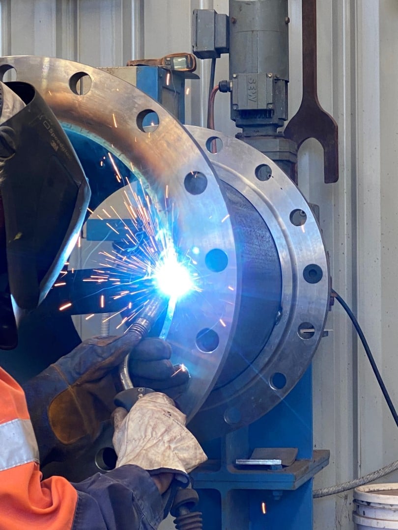 Twomeys welder running a weld on a large flanged pipe spool mounted on a positioner