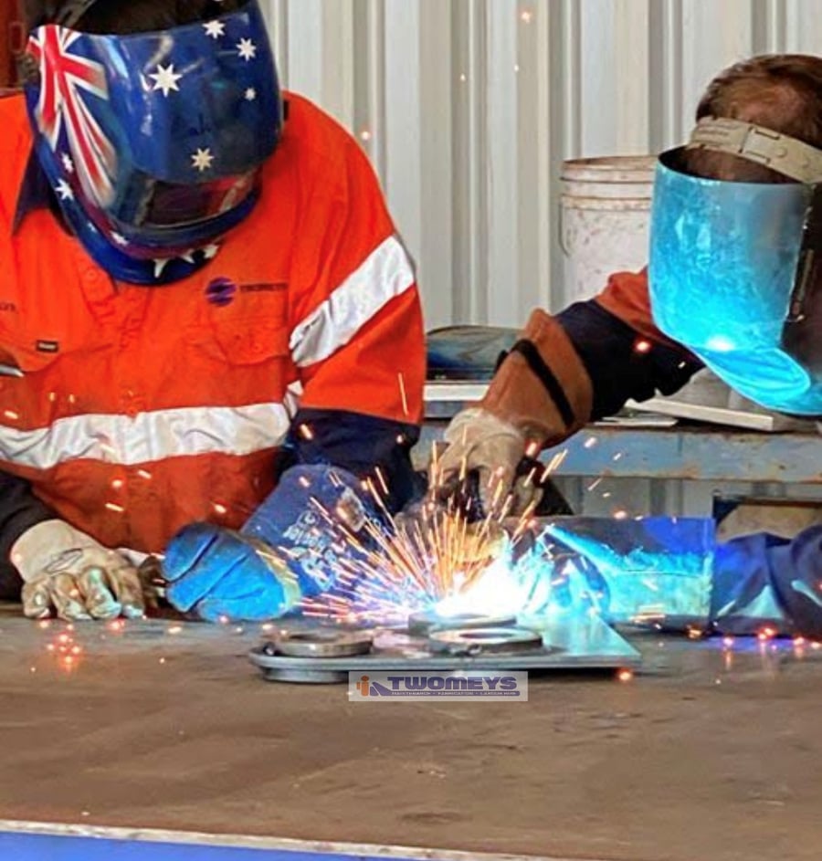 Two Twomeys boilermakers welding a flanged steel plate, sparks flying from the weld