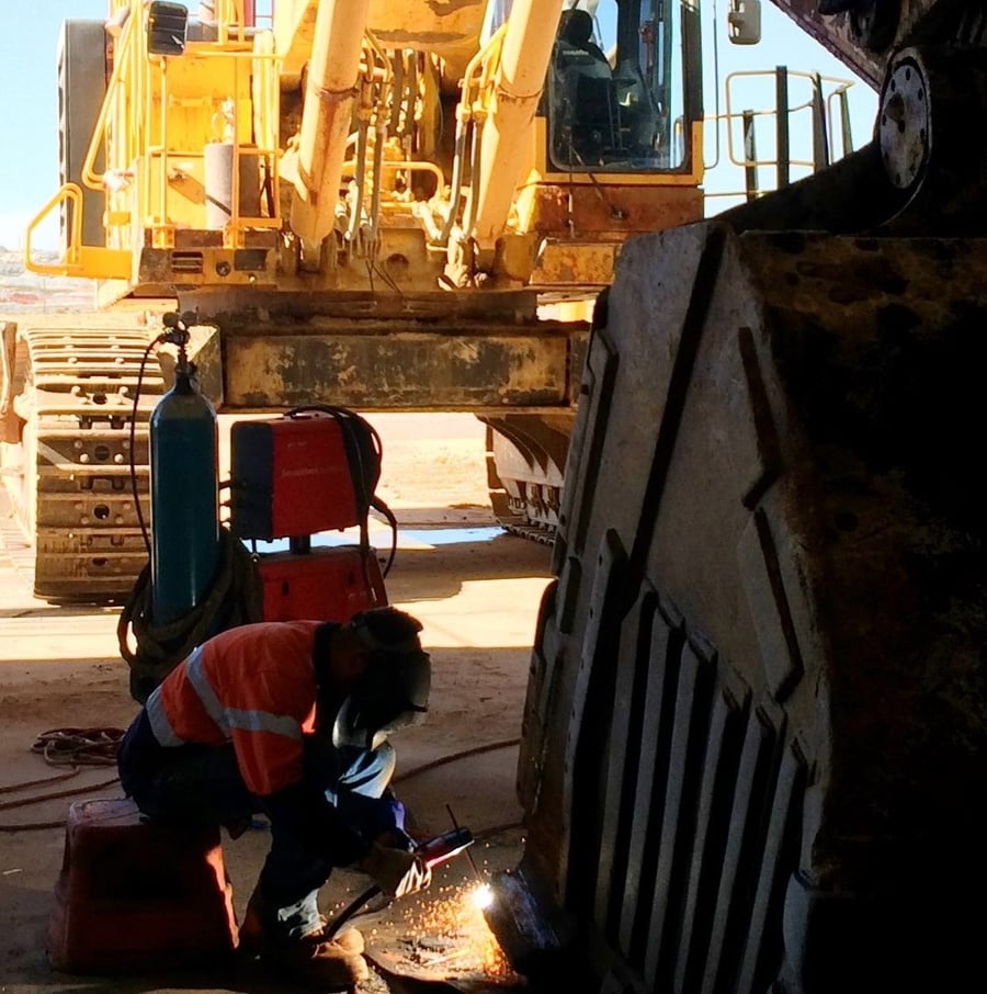 Twomeys tradesperson gouging a repair on an excavator bucket on site, with the excavator standing behind