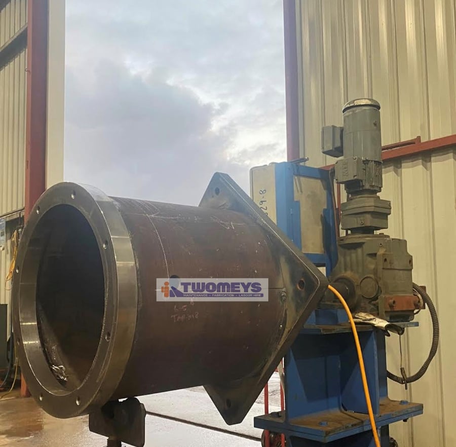 Large fabricated steel housing with a machined flange, mounted on a welding positioner in the workshop
